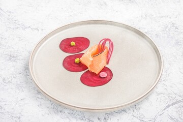 An elegant salmon creation rests on beet rounds, with accents of vibrant green and pink, presented...