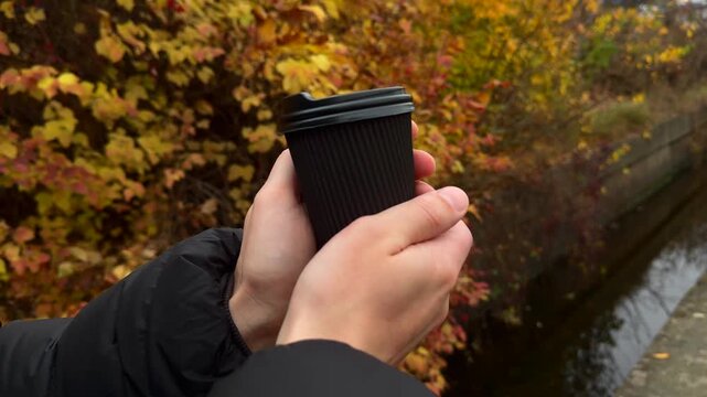 A black glass with a hot drink on the tipple against the background of yellow autumn trees.