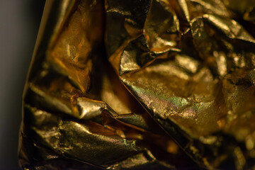 A detailed macro photo of a golden-colored shining chocolate wrapper, capturing texture, light reflection, and luxurious appeal.