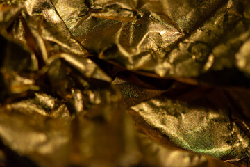 A detailed macro photo of a golden-colored shining chocolate wrapper, capturing texture, light reflection, and luxurious appeal.