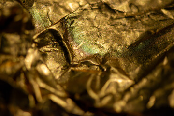 A detailed macro photo of a golden-colored shining chocolate wrapper, capturing texture, light reflection, and luxurious appeal.