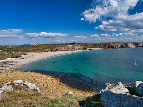Wide-angle view of a clear turquoise cove, sandy beach and rocky cliffs near Pointe de Pen-Hir on the Crozon Peninsula, Brittany, France, under a bright blue sky.