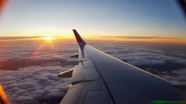 Airplane wing view during a flight above the clouds at sunrise with a bright sun and clear blue sky