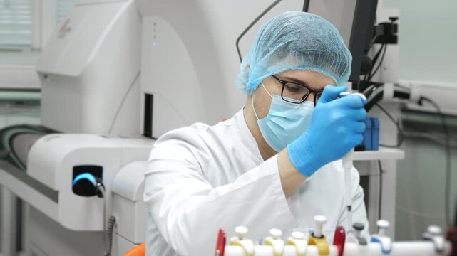 Medical scientist in protective mask and gloves using micropipette in modern laboratory during medical research under bright laboratory light.