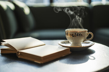 A cup of hot tea or coffee stands on the table next to a thick book.
