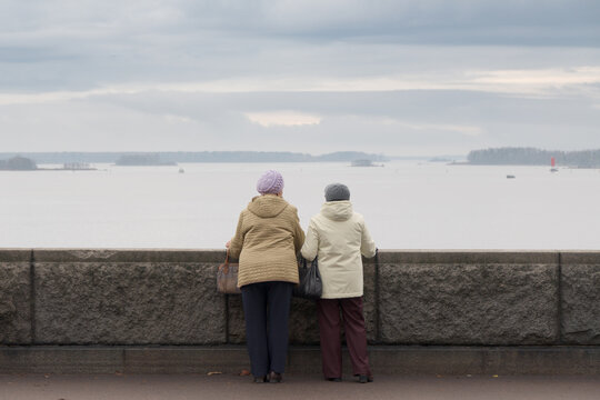 Two elderly friends admire the view from the embankment. View from behind. Cloudy autumn day.