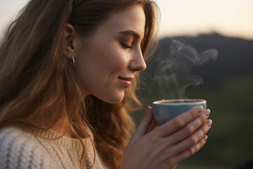 A beautiful woman with lush hair inhales the aroma of fresh coffee.