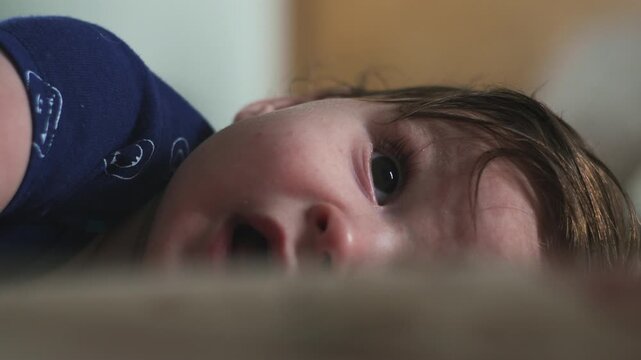 Close-up of baby lying on side, expressive eyes and soft lighting capturing tenderness and curiosity in intimate home moment