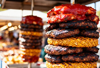 Close up shot of stacked grilled burger patties and pineapple slices on a metal skewer stand