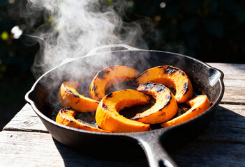 Steaming squash slices in a cast iron skillet on a wooden surface in outdoor sunlight