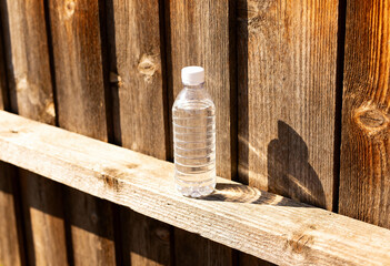 A clear plastic water bottle with a white cap sits on a wooden beam near a wooden fence