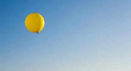 Single yellow balloon floating freely against a clear blue sky background