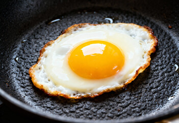 A single fried egg with a bright yellow yolk sits in a black cast iron frying pan close up