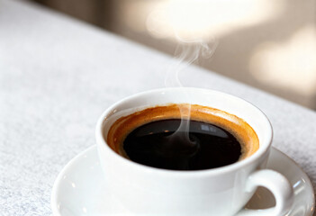 A close up shot of a white cup of black coffee with steam rising on a white surface area