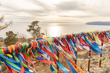 Vibrant ribbons tied near Lake Baikal flutter along a railing overlooking a rocky coastline.  Spiritual or shamanic offering to make wishes and show respect to spirits.