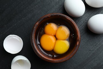Raw eggs and yolks on black table, flat lay
