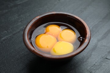 Fresh egg yolks in bowl on black table, closeup