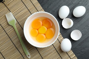 Raw eggs, yolks and brush on black table, flat lay