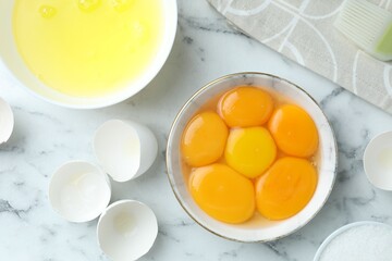 Broken eggs, yolks and whites on white marble table, flat lay