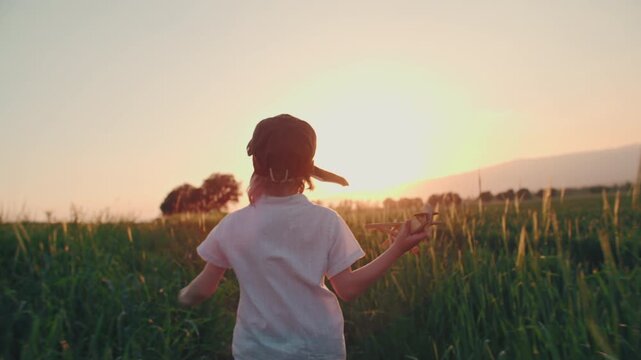boy in pilot hat running through field holding wooden airplane above head cinematic slow motion concept of childhood dream freedom adventure imagination and happiness golden sunset
