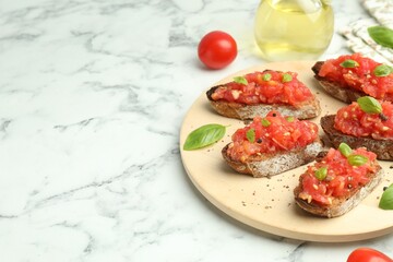 Tasty bruschettas with tomatoes and basil on white marble table, closeup. Space for text