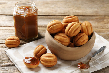 Tasty nut shaped cookies with boiled condensed milk on wooden table, closeup