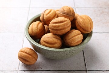 Delicious nut shaped cookies with boiled condensed milk in bowl on light tiled table, closeup
