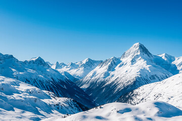 Obraz premium High-resolution photograph of majestic snow-covered mountain peaks under a clear blue sky. The sunlight enhances the crisp contrast between the bright snow and deep shadows of the alpine valley.
