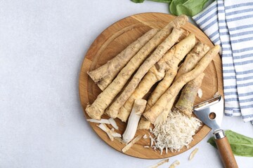 Whole and grated horseradish roots near peeler on light grey table, top view. Space for text