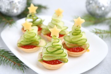 Obraz premium Christmas tree shaped tartlets made with red caviar, cucumber, cheese and festive decor on white table, closeup