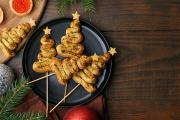 Christmas tree shaped snacks made with puff pastry, pesto sauce, cheese and festive decor on wooden table, flat lay. Space for text