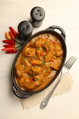 Salt, pepper shakers, chili and chicken tikka masala on wooden table, flat lay