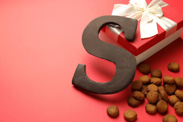 Saint Nicholas (Sinterklaas) day. Chocolate letter S, kruidnoten cookies and gift box on red background, closeup. Space for text