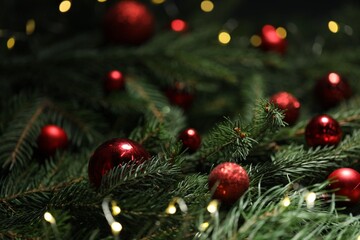 Beautiful spruce tree branches with Christmas ornaments and blurred lights as background, closeup. Bokeh effect