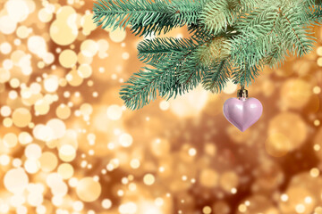 Christmas tree branch with heart-shaped ball against blurred lights, bokeh effect