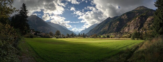 Panoramic view of a valley with a bright green field flanked by mountains under a cloudy sky