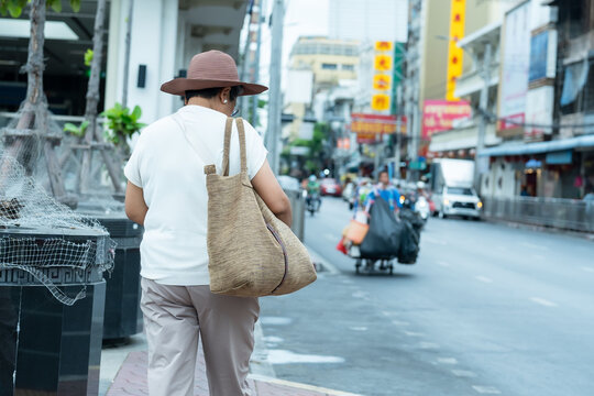 Senior asian women travelers walking down busy asian street carrying bags and drinks enjoying adventure showing friendship relaxation and joyful retirement lifestyle