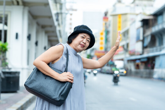 Senior asian woman traveler waving and smiling on street showing happiness friendliness and freedom representing joy and active retirement lifestyle during travel and exploration