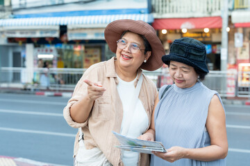Joyful senior asian female travelers checking map and smartphone on street pointing direction laughing together enjoying retirement lifestyle travel exploring city culture vacation friendship journey