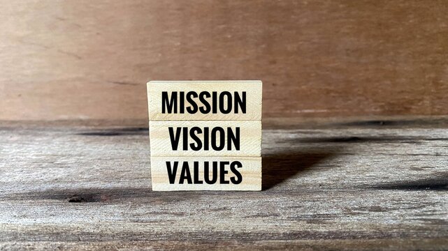 Stacked wooden blocks spelling 'Mission, Vision, and Values' on a wooden surface. Represents the foundational strategy and core identity of any business or organisation.