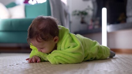 Baby lying on floor in green outfit, looking down with calm curiosity, peaceful moment of exploration and early sensory learning at home