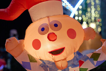 A cheerful inflatable clown with a red nose and Santa hat smiles at a holiday event. Colorful diamond patterns and bright lights glow at night.