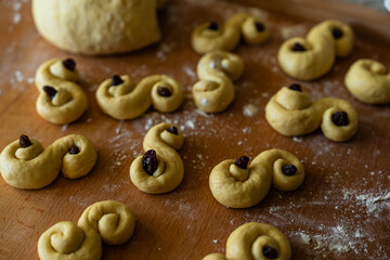 Process of making traditional Swedish saffron buns. S-shaped yeast buns spiced with saffron and decorated with raisins on wooden board.