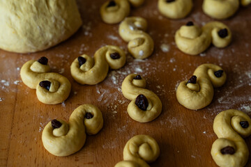 Process of making traditional Swedish saffron buns. S-shaped yeast buns spiced with saffron and decorated with raisins on wooden board.