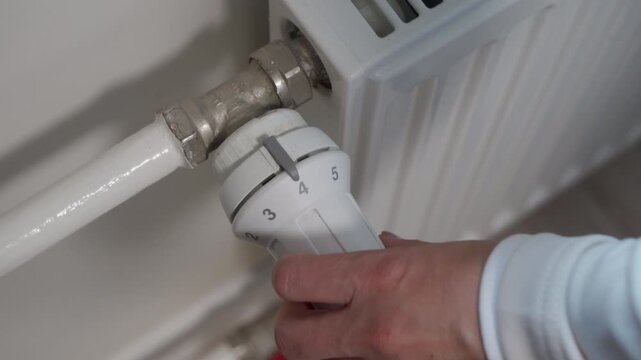 The Satisfying Clicks of Comfort: Hand Adjusts Radiator Thermostat at Home.