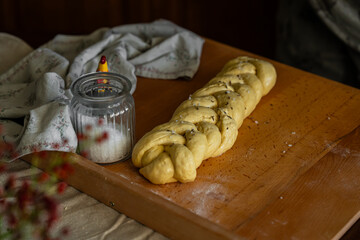 Unbaked challah bread sprinkled with sea salt flakes and cumin on wooden board.