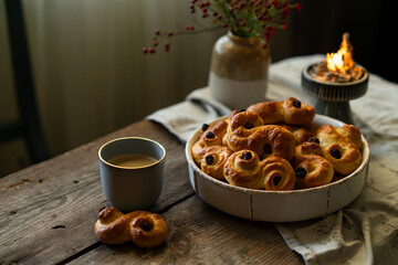 Homemade Swedish saffron buns and coffee on wooden table. Traditional treat eaten on Saint Lucia Day and during Advent. Spiced with saffron and decorated with raisins.