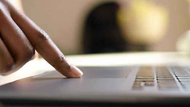 An extreme close-up video of a warm brown hand precisely tapping a dark grey laptop touchpad with soft bokeh, highlighting focused digital interaction and productivity - Powered by Adobe