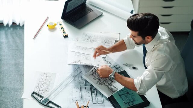 Architect engineer using laptop planning house design at office while sitting at meeting table with blueprint and equipment scatter around.Skilled civil engineer working at blueprint. Alimentation.