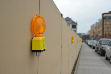 Warning lamps on a construction site fence with parked cars